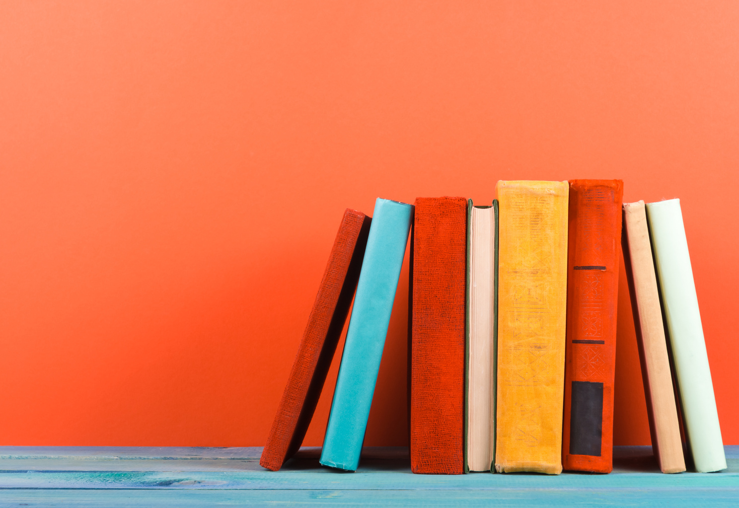 Row of colorful hardback books, open book on red background